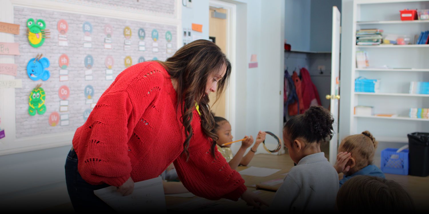 Teacher helping students with their work at a classroom table.