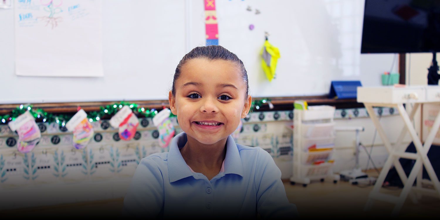 Young student smiling in a classroom decorated with holiday stockings.