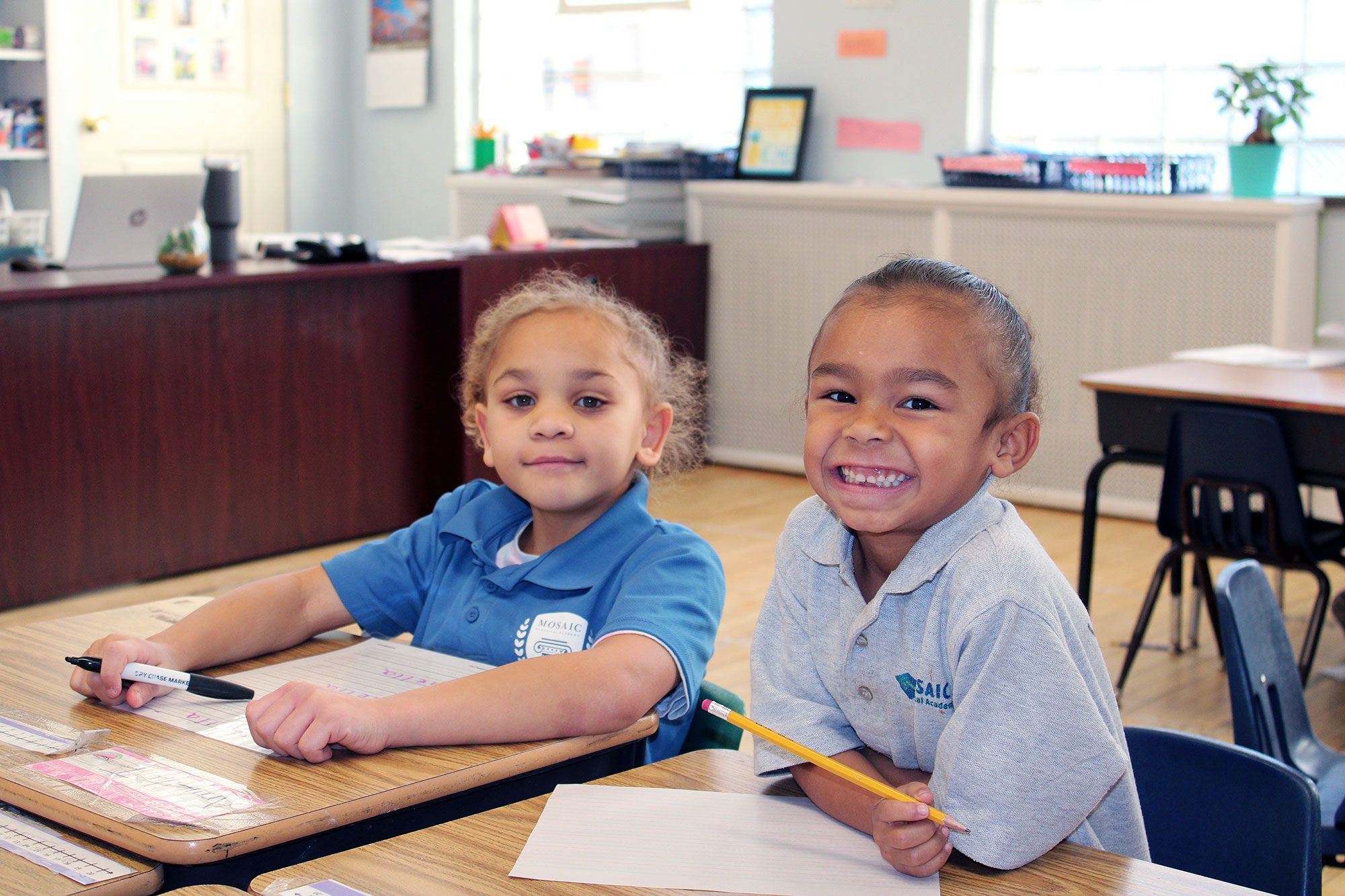 Two smiling students working at their desks in a classroom.